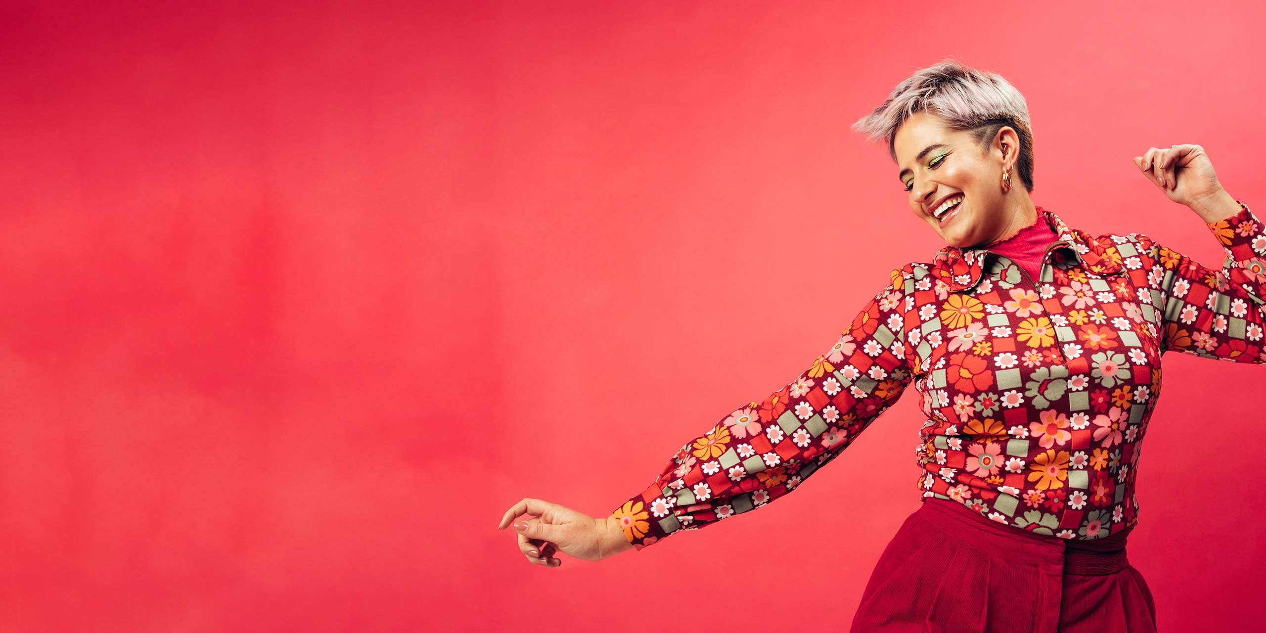Farbenfrüh gekleidete Frau freut sich und tanzt vor einem roten Hintergrund